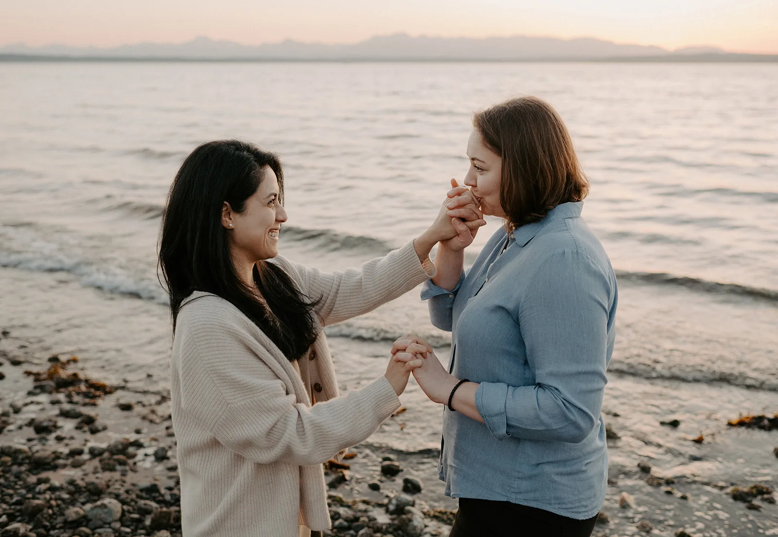 a couple shares sweet hand kisses while having their engagement session at carkeek park