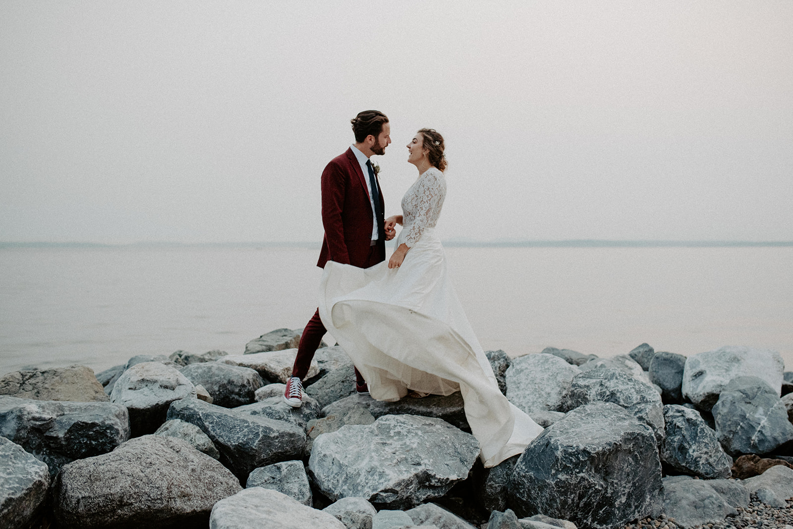 A couple stands on rocky shores at Pocket Beach in Seattle, sharing a joyful moment with the serene water in the background.