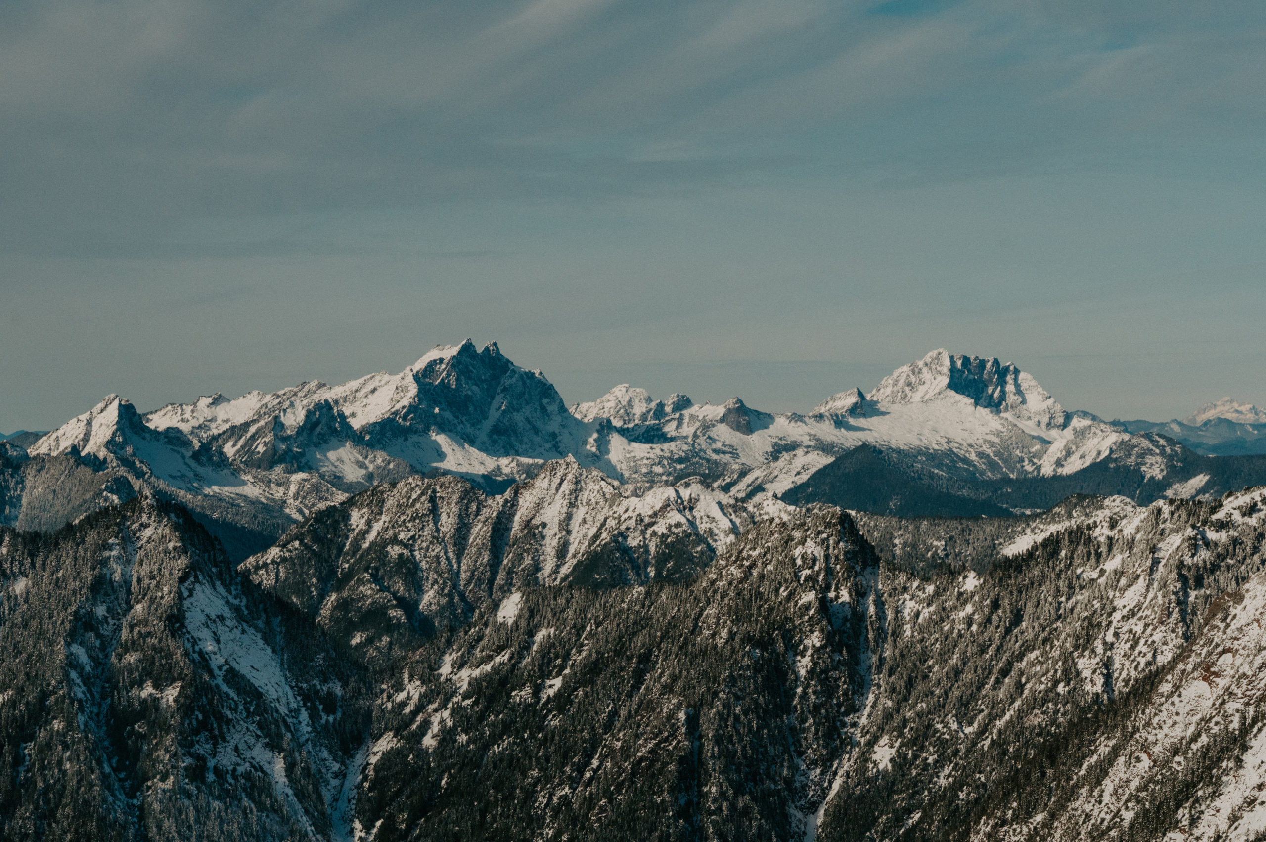 A panoramic view of snow-covered jagged peaks in the Cascade Mountains under a soft winter sky.