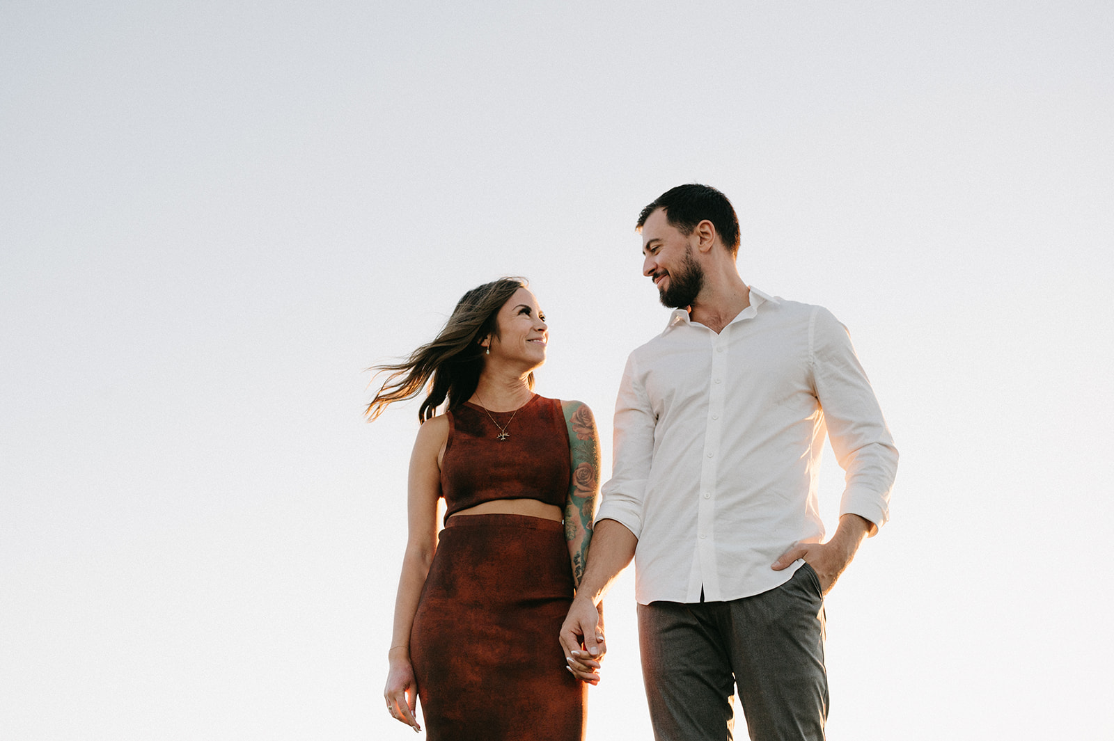 A couple holding hands and smiling at each other against a clear sky.