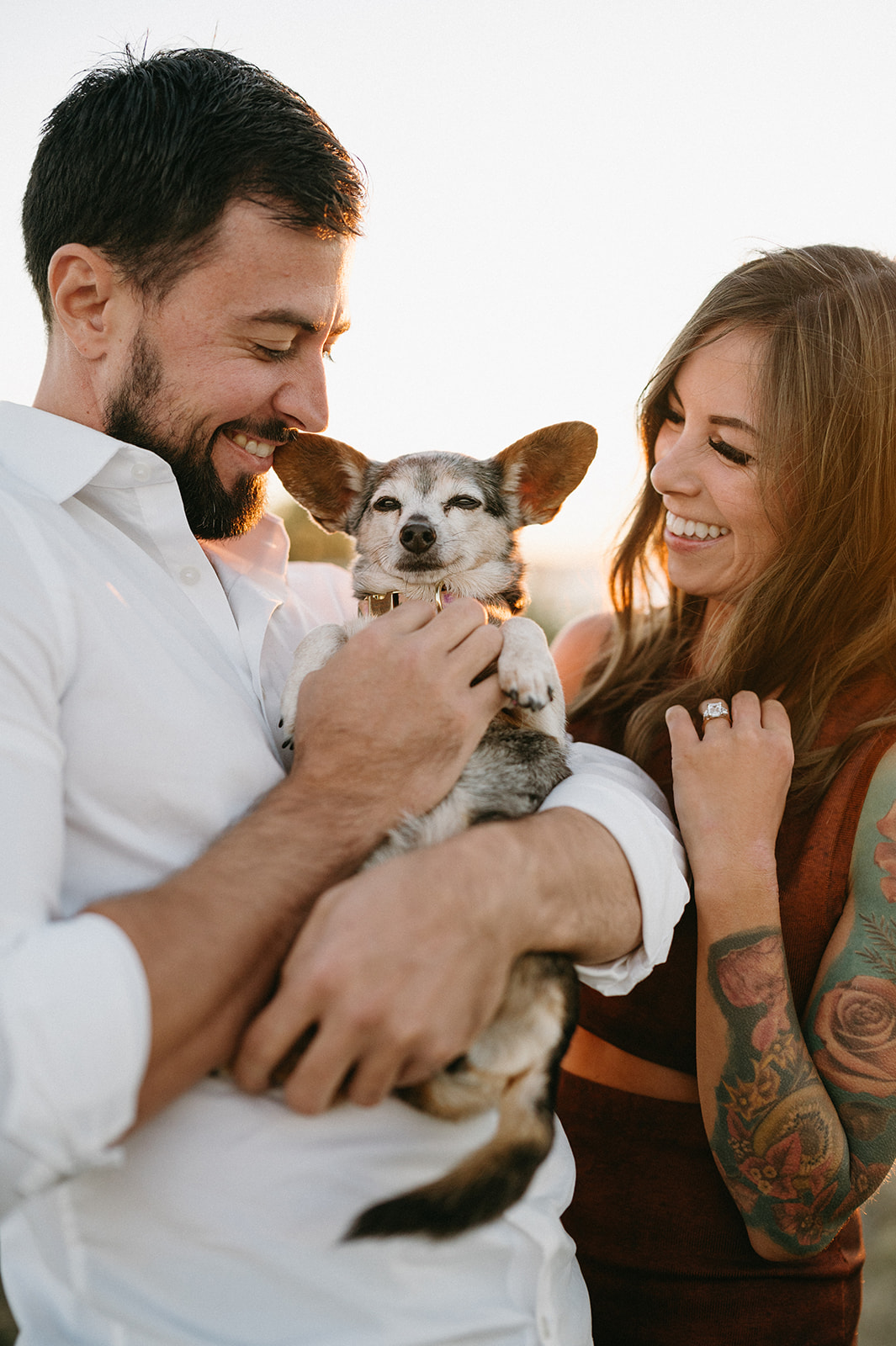 A man holding a small dog while a woman looks at them lovingly.