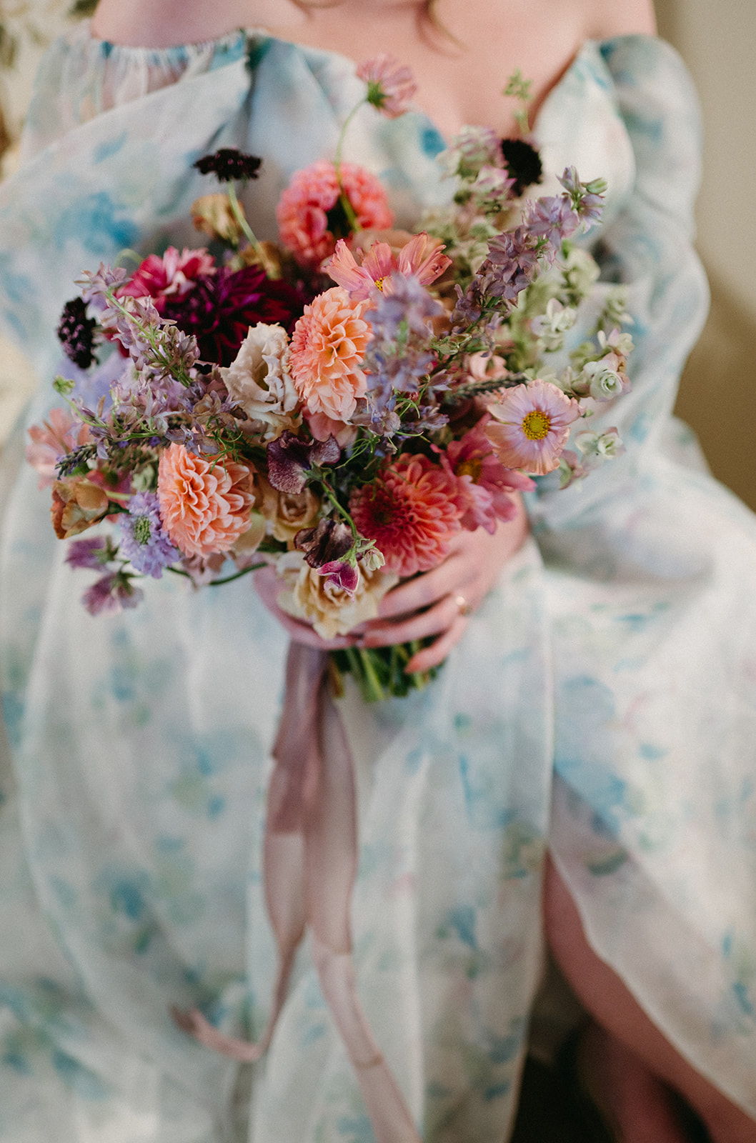 Close-up of pastel floral bouquet held against a watercolor-inspired gown