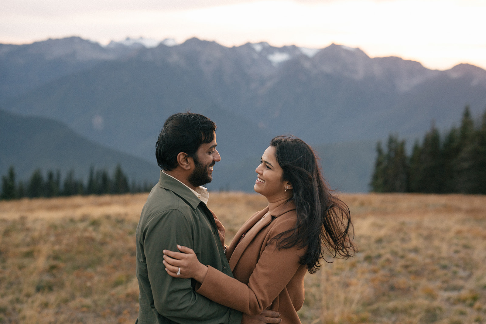 Couple laughing and holding each other with mountains fading into the distance.
