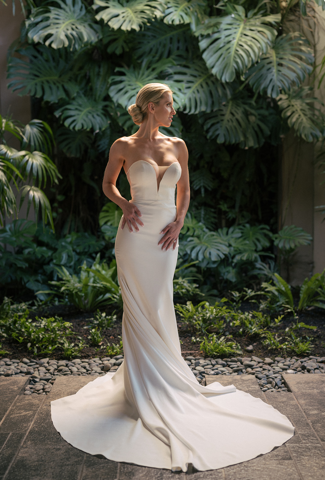 Bride standing in front of large monstera leaves in her fitted wedding gown in Maui.
