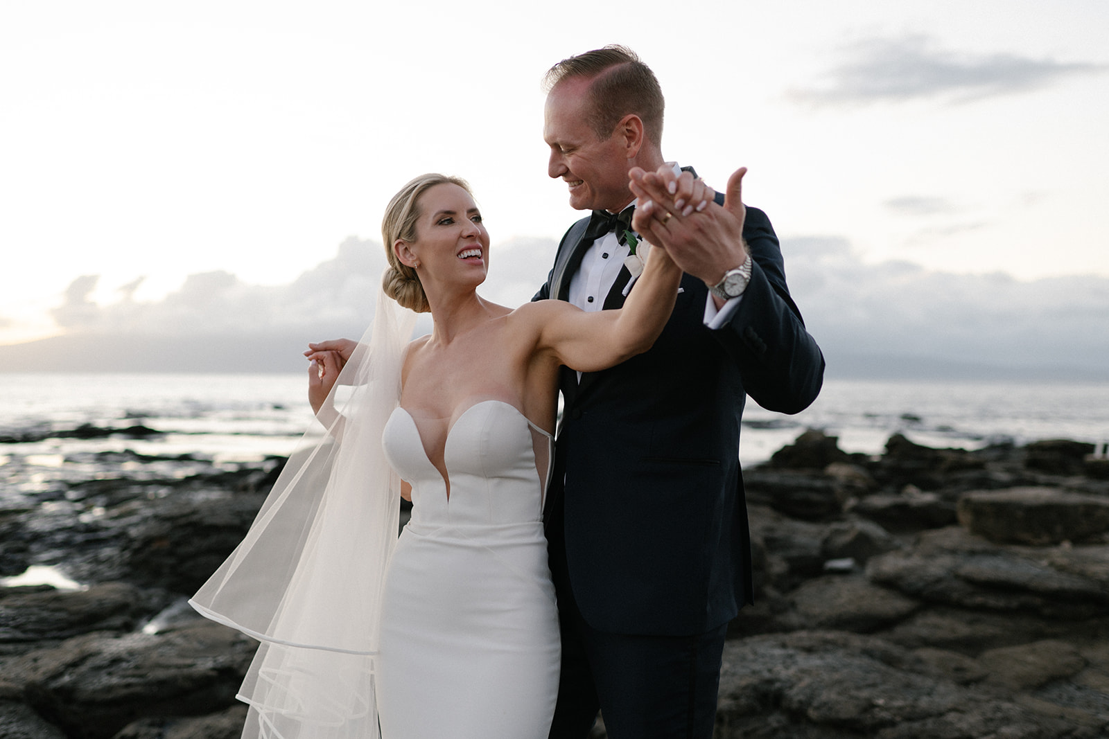 Bride and groom dancing together on the lava rocks at sunset along the Kapalua coastline in Maui.
