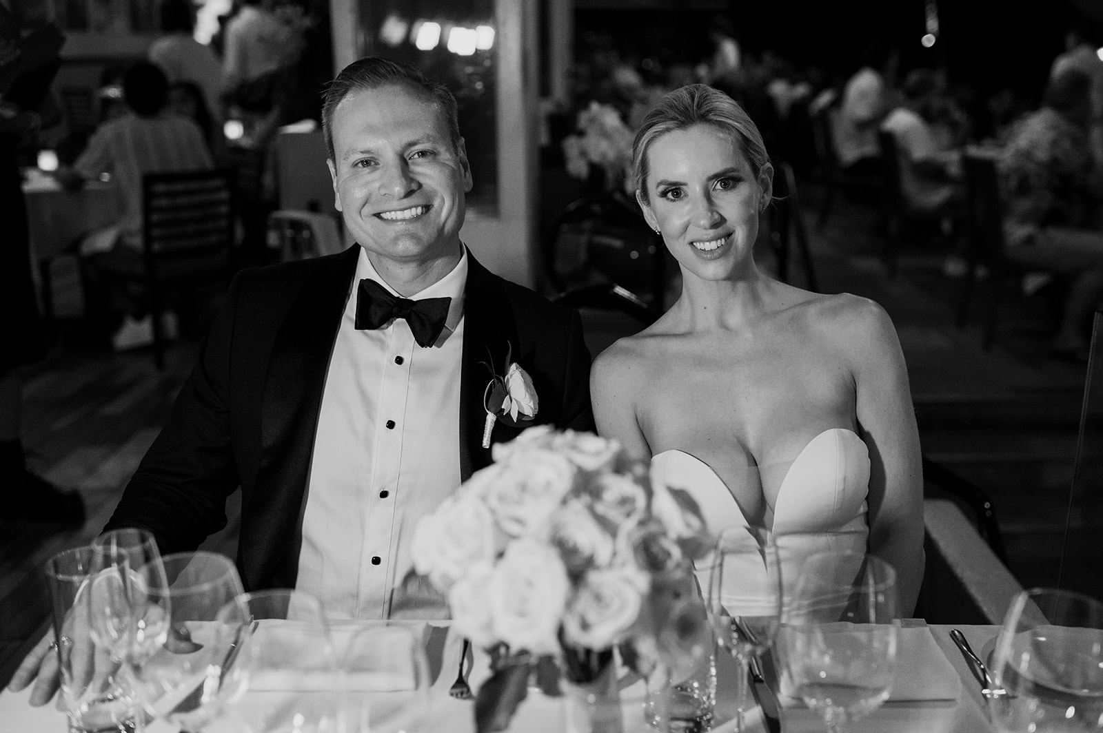 Black and white portrait of the bride and groom seated together at their table during dinner at Merriman’s Kapalua.
