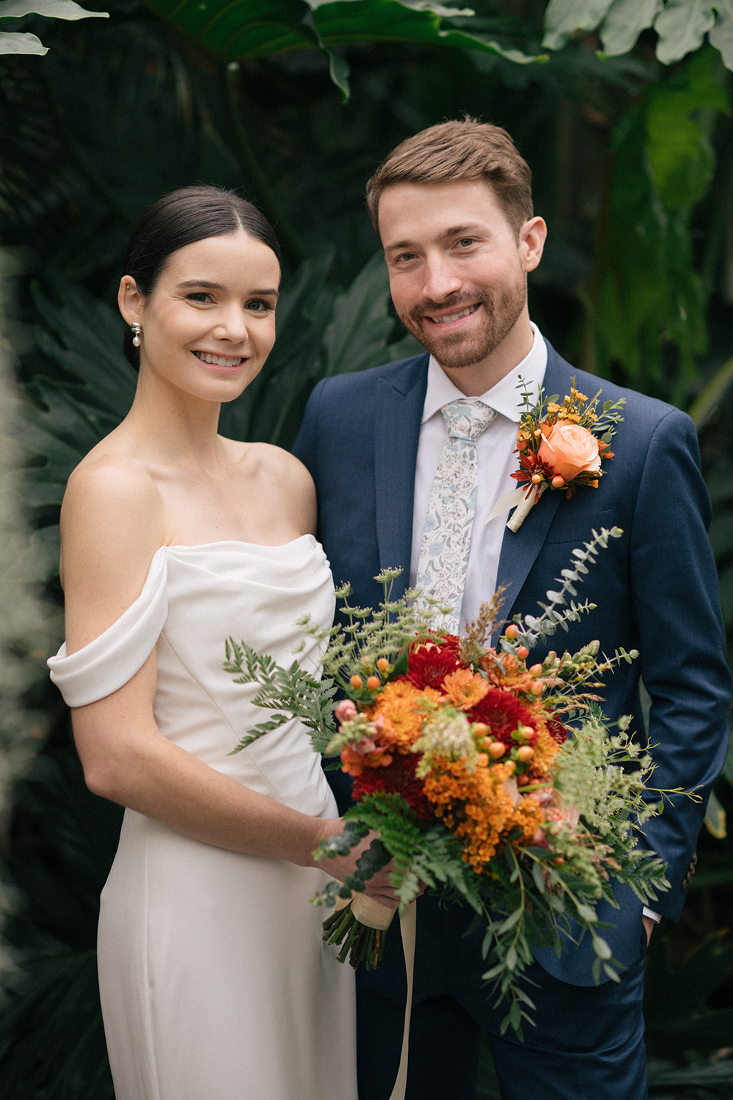 Taylor and Patrick smiling together with a vibrant bouquet in the lush greenery of the Seymour Conservatory.