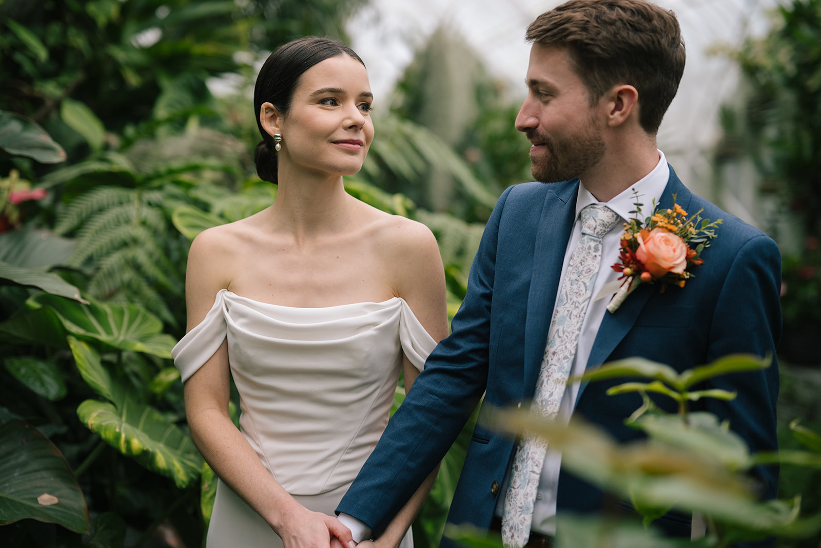 Taylor and Patrick holding hands while sharing a loving glance in the lush greenery of the Seymour Conservatory.