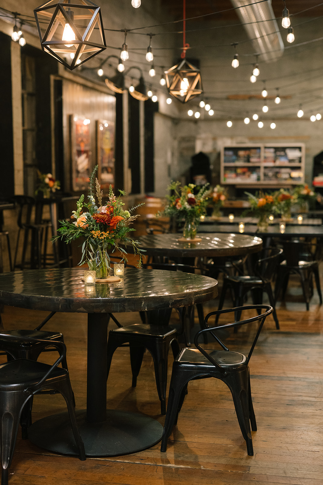 Reception tables decorated with floral arrangements and candles under string lights.