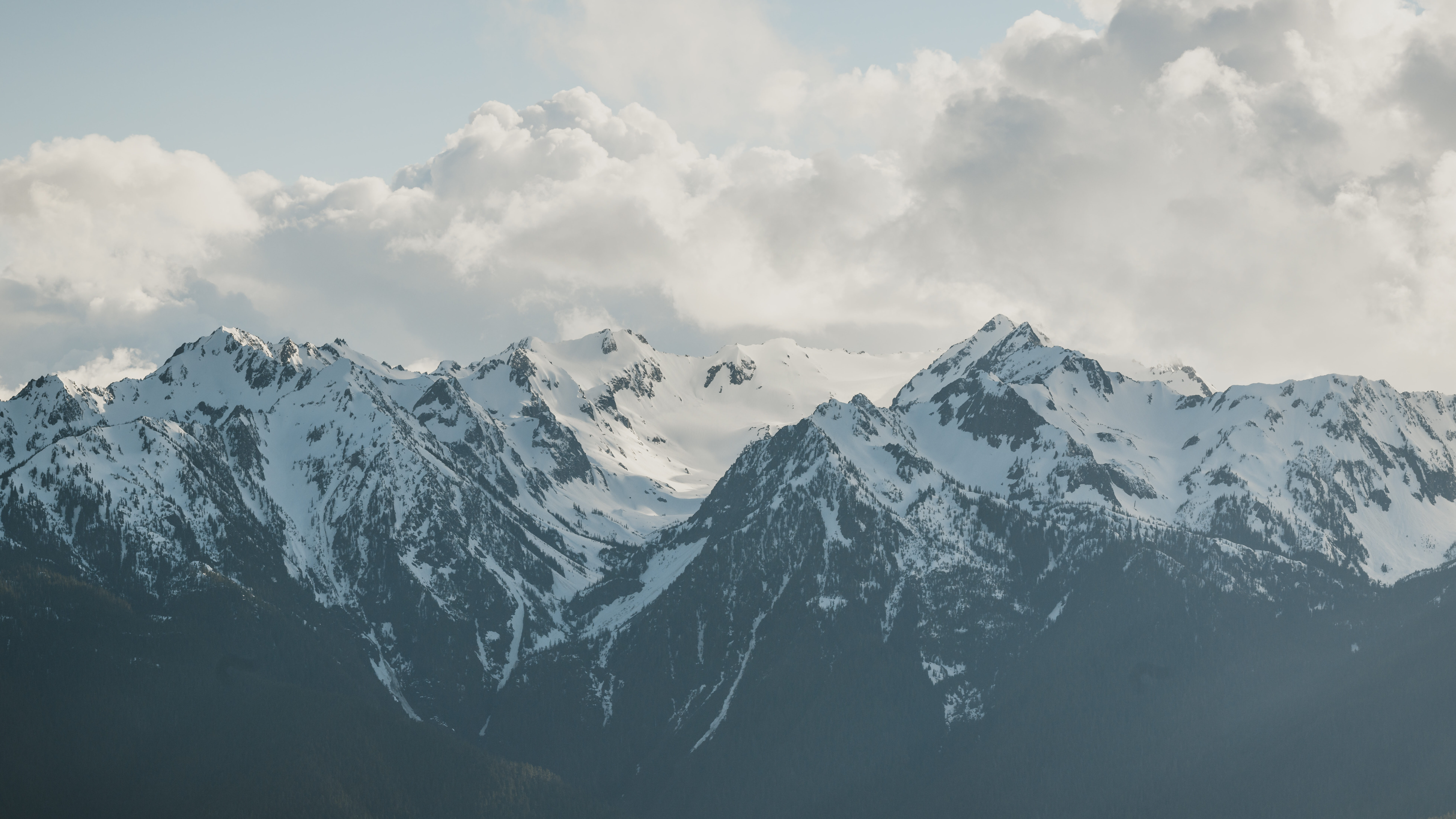 Snow-capped peaks of the Olympic Mountains under a cloudy sky in Washington.
