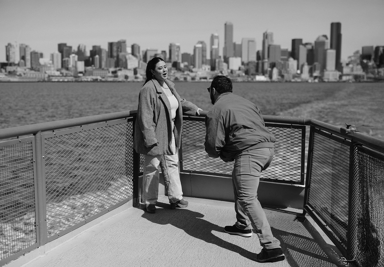 Johnny kneels in front of Alyssa during a ferry proposal with the city in the background