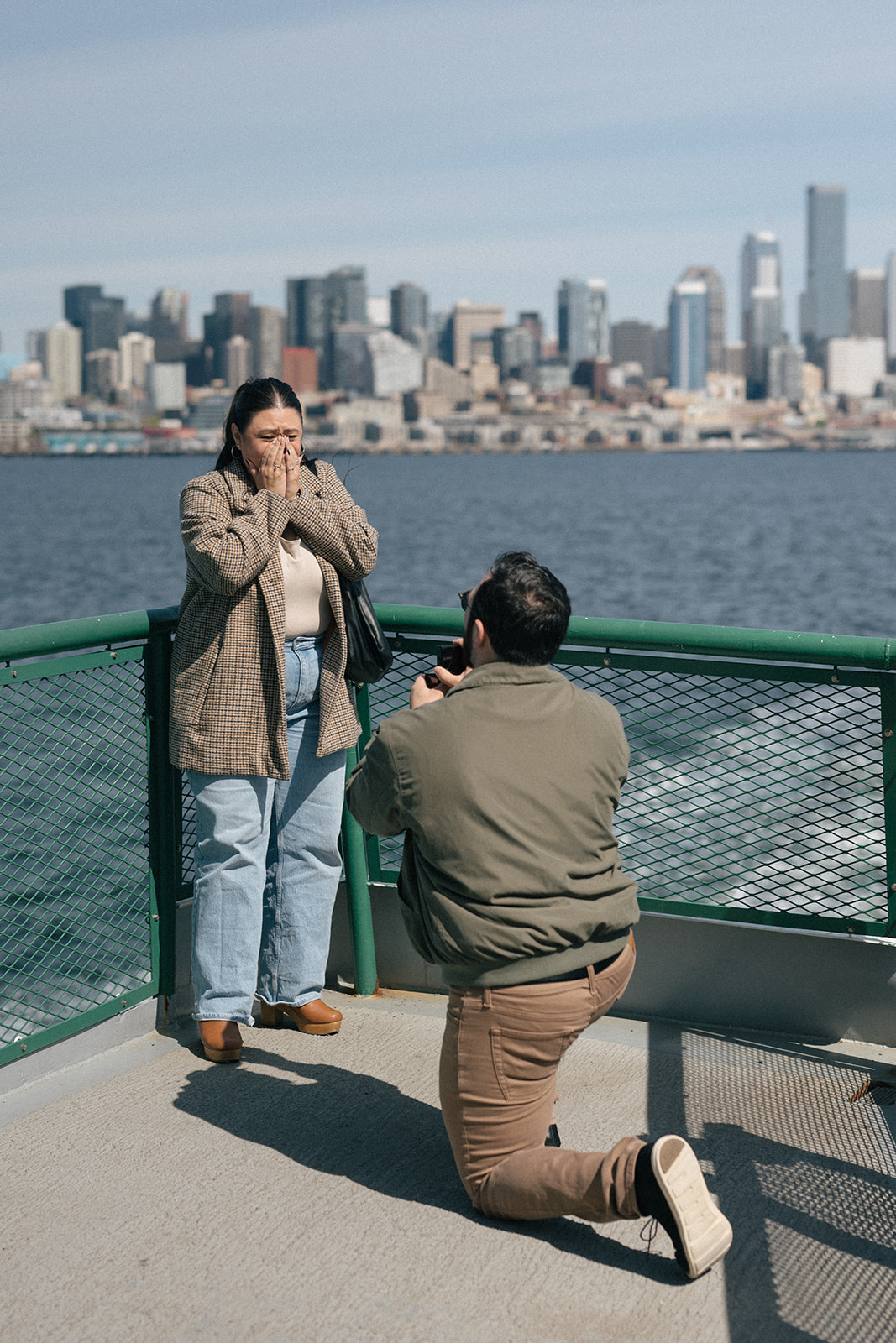 Johnny kneels in front of Alyssa during a proposal on the ferry deck