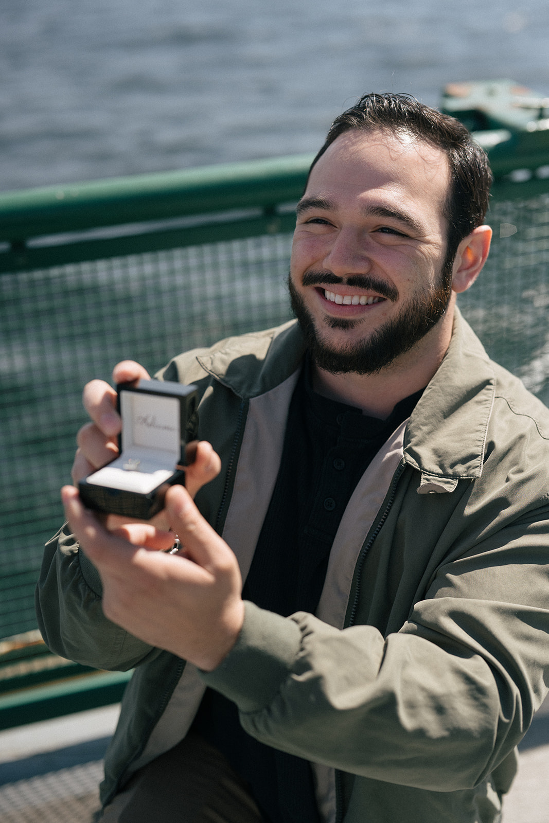 Johnny smiles while holding out the open ring box on the ferry