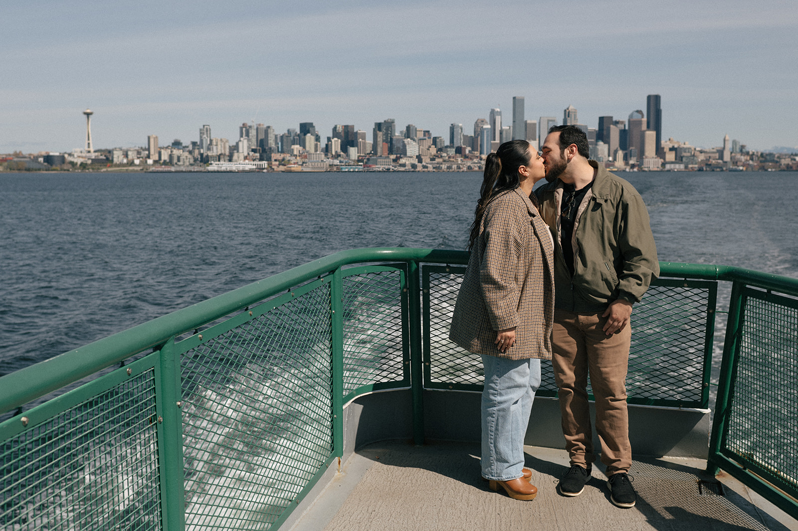 Johnny and Alyssa share a kiss at the edge of the ferry with the Seattle skyline and Space Needle in the background.