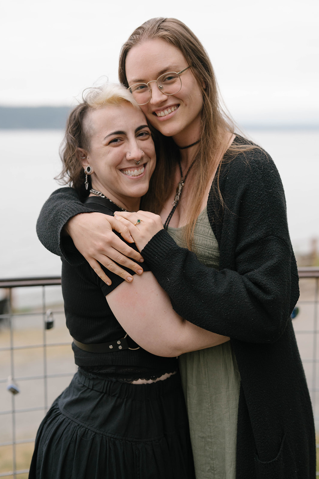 Two women embracing and smiling at a scenic overlook on Whidbey Island with Puget Sound in the background.