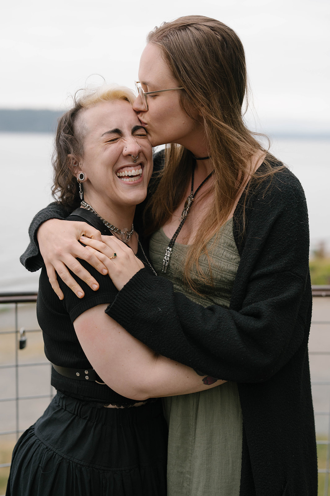 One woman kisses her partner’s forehead as they laugh together after a proposal at a Whidbey Island viewpoint.