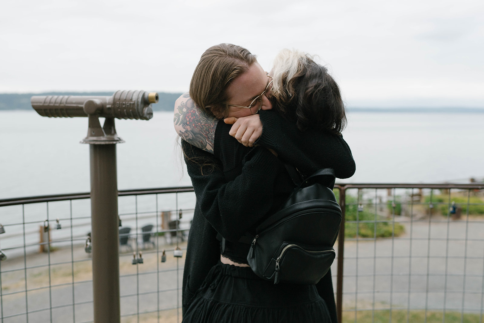 Two women embracing at a whale watching overlook on Whidbey Island after a surprise proposal, with Puget Sound in the background.
