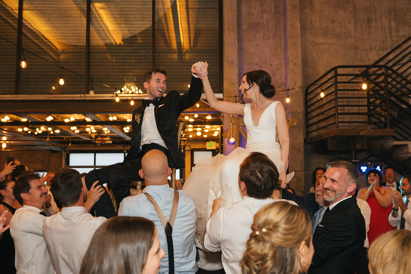 Bride and groom raised on chairs while holding hands during the horah at their Fremont Foundry wedding reception