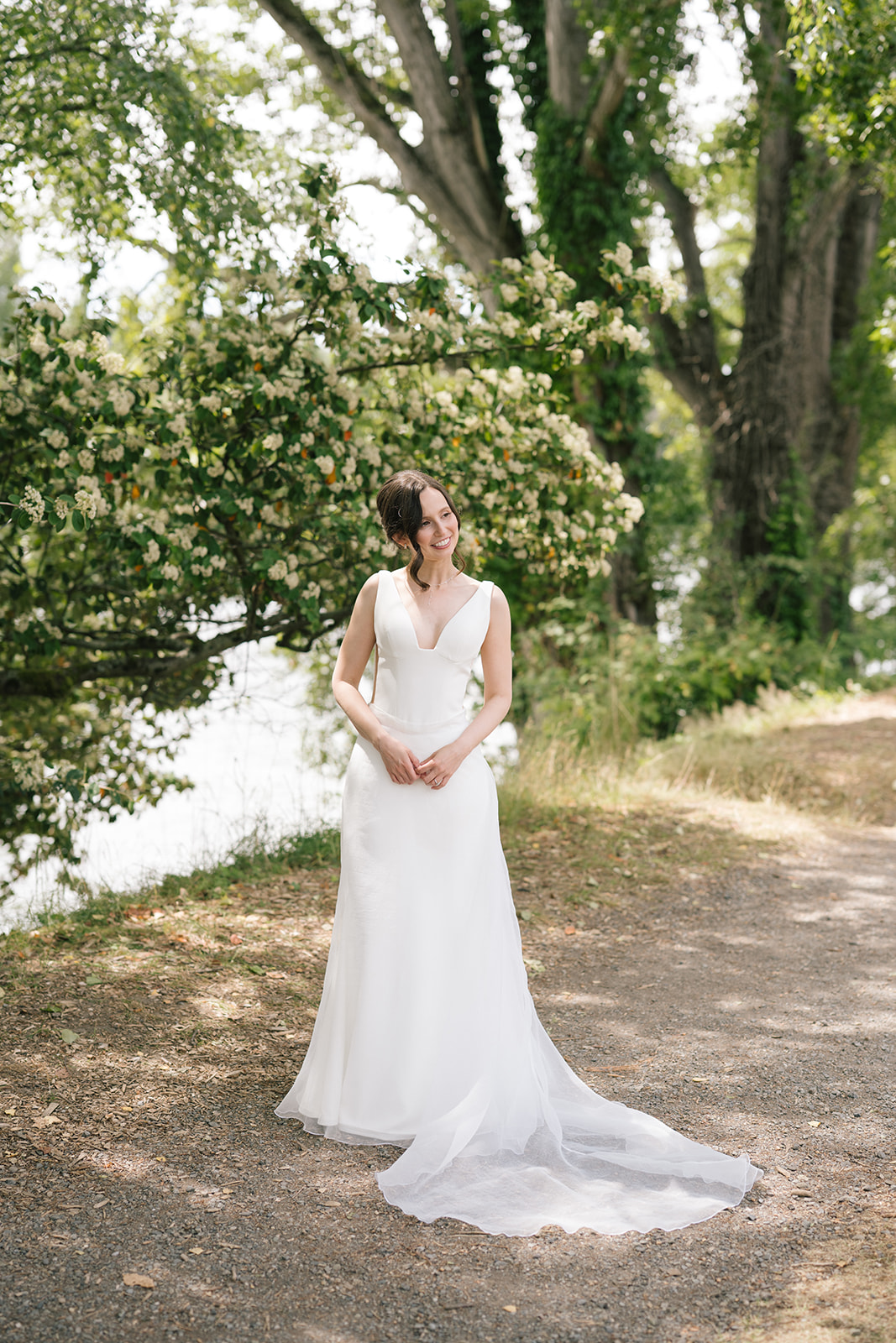 Bride standing alone under blooming trees along the waterfront near the Fremont Foundry in Seattle