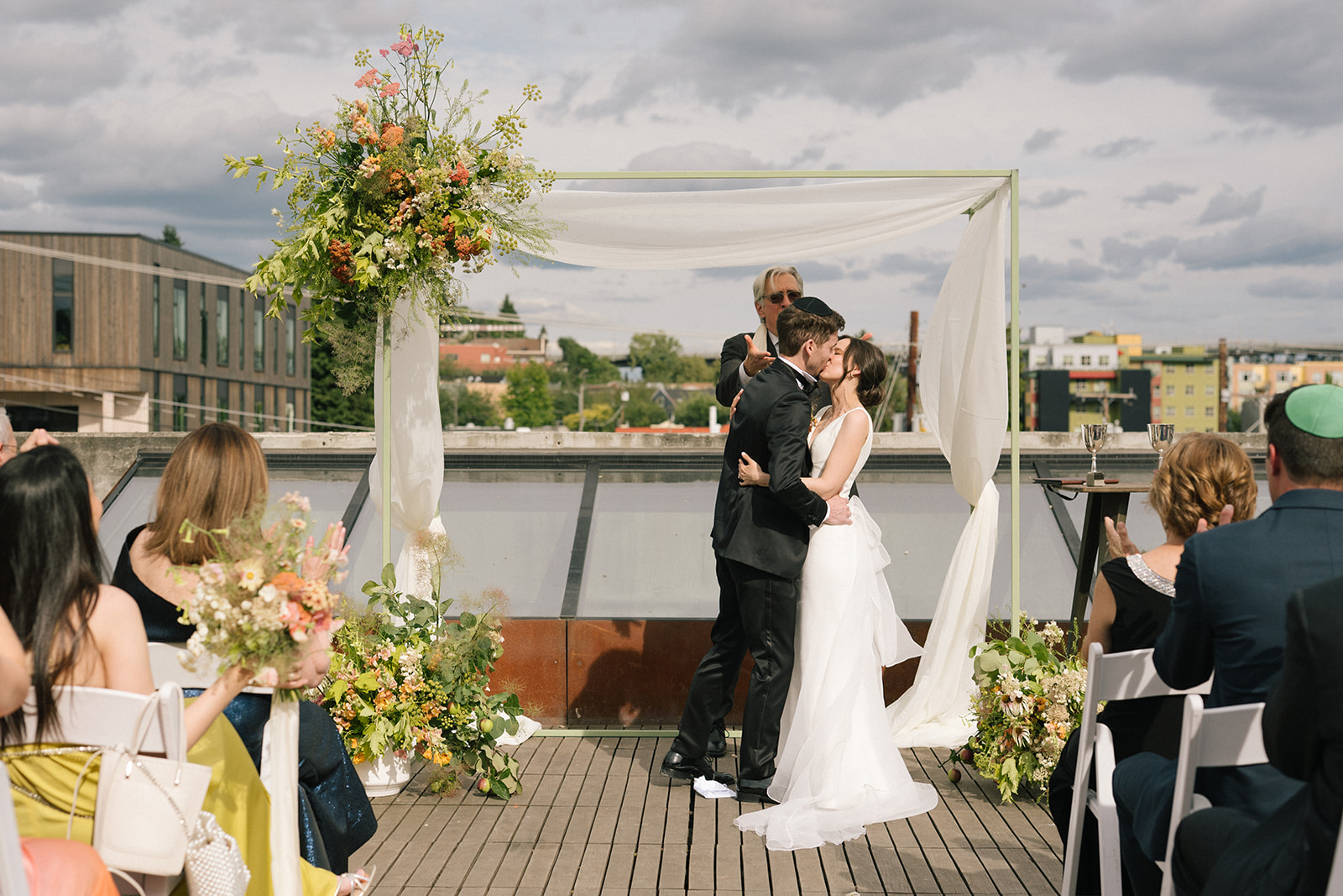 Bride and groom sharing their first kiss under a floral arch during their rooftop ceremony at the Fremont Foundry
