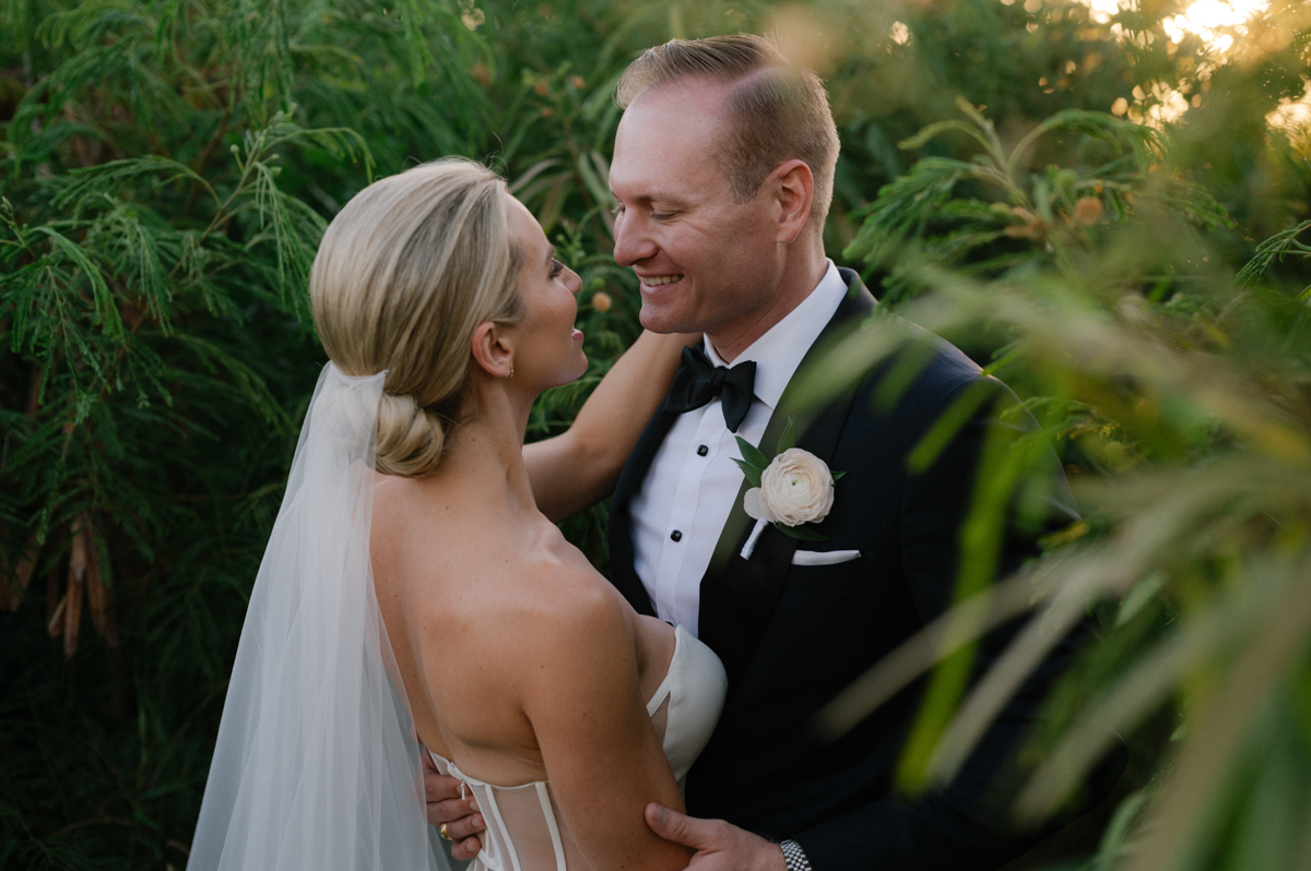 Bride and groom embracing in lush tropical greenery during golden hour in Kapalua, Maui.

