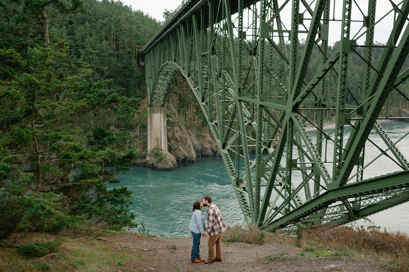 Jonathan and Ashley share a quiet kiss beneath the Deception Pass bridge overlooking the water.