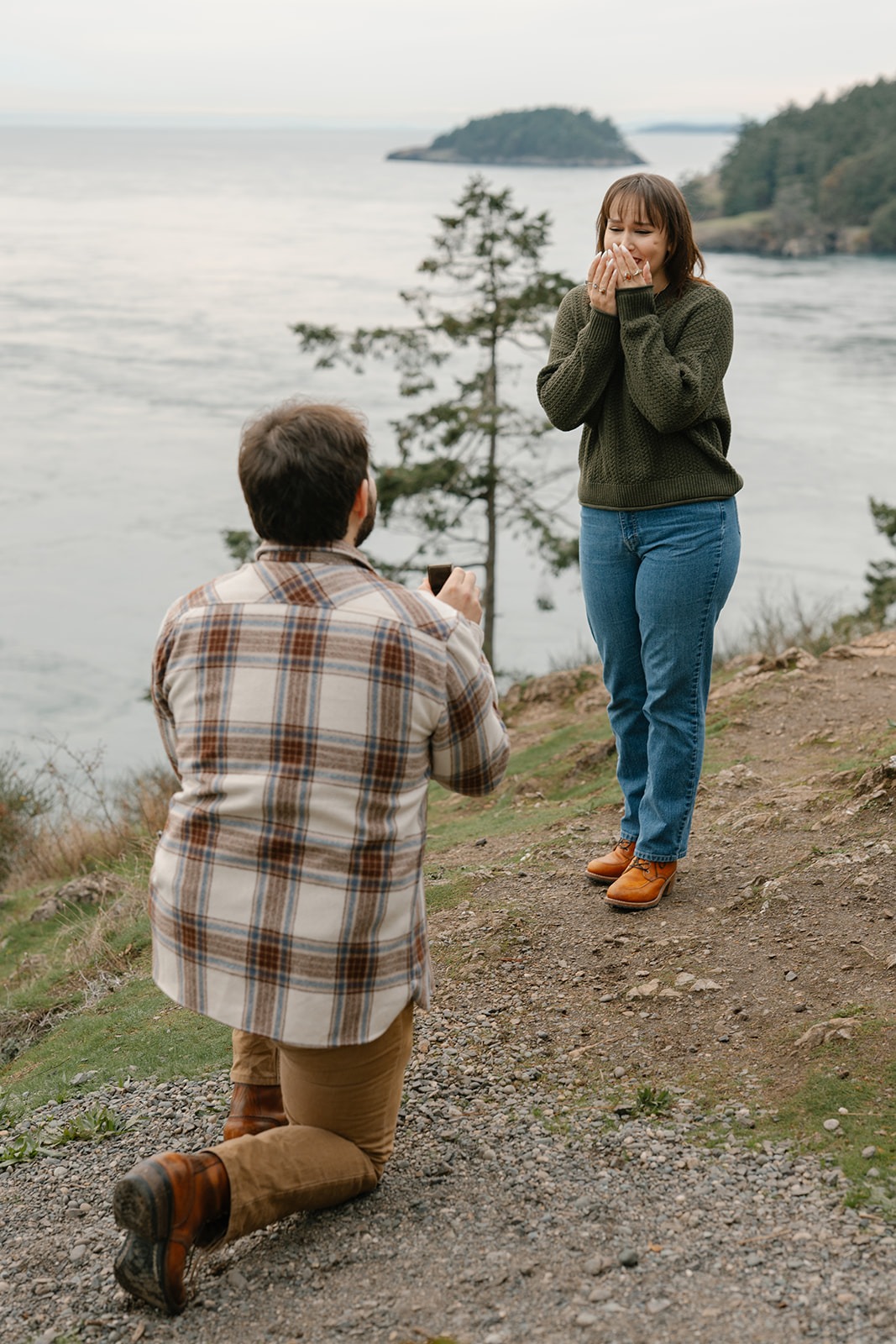 Ashley covers her mouth in surprise and emotion as Jonathan proposes by the water.