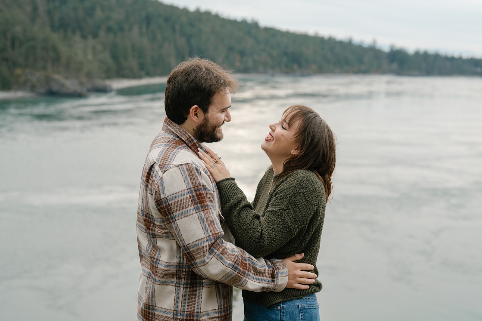 Jonathan and Ashley laugh together while standing by the water at Deception Pass after their proposal.