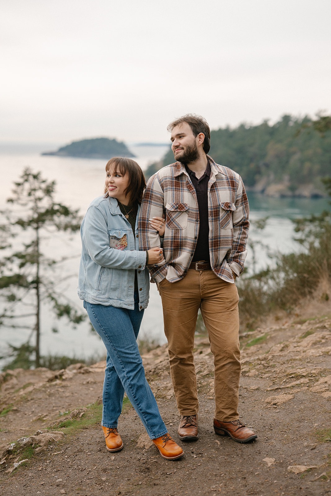 Jonathan and Ashley stand close together on the cliffside overlooking the water at Deception Pass.