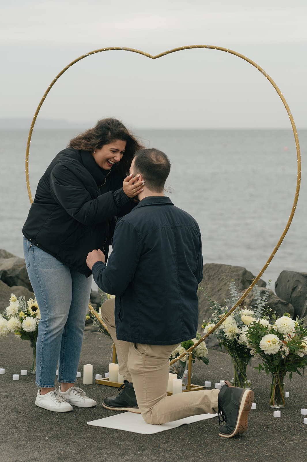 Brad kneels beneath a heart-shaped arch, holding Aysha’s hands as he asks her to marry him by the water.