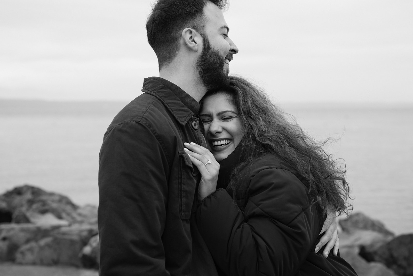 Brad and Aysha hold each other and smile in a quiet black and white portrait after getting engaged.