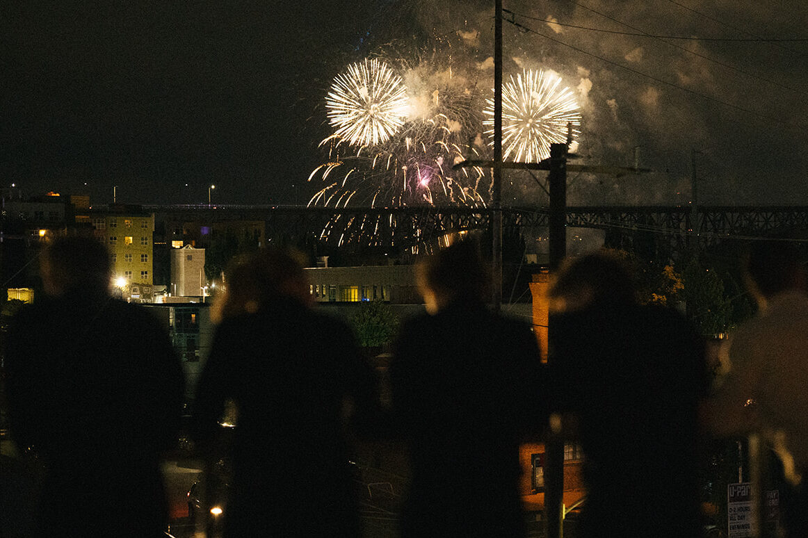 Wedding guests silhouetted on a rooftop watching Fourth of July fireworks over Lake Union and the Fremont Bridge