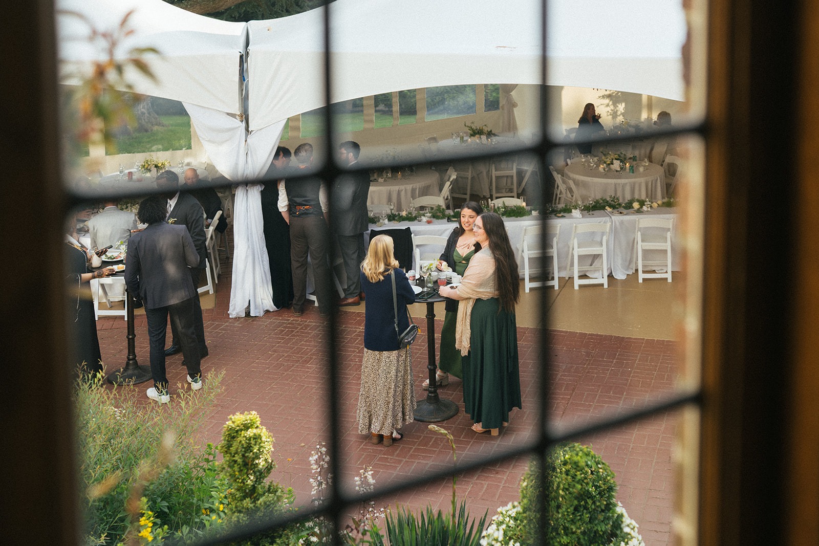 Guests socializing at cocktail tables viewed through a window at Lairmont Manor