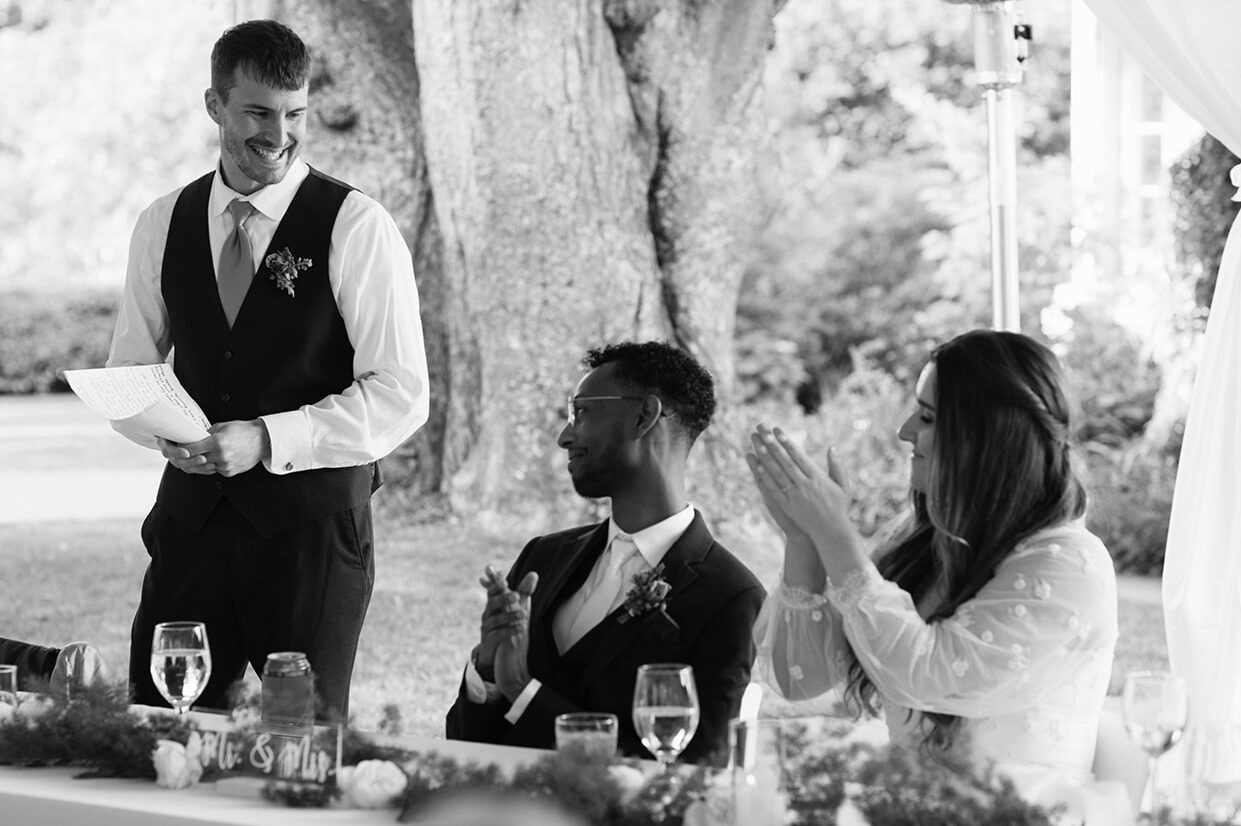 Wedding guests applauding during reception speeches inside a tent at Lairmont Manor