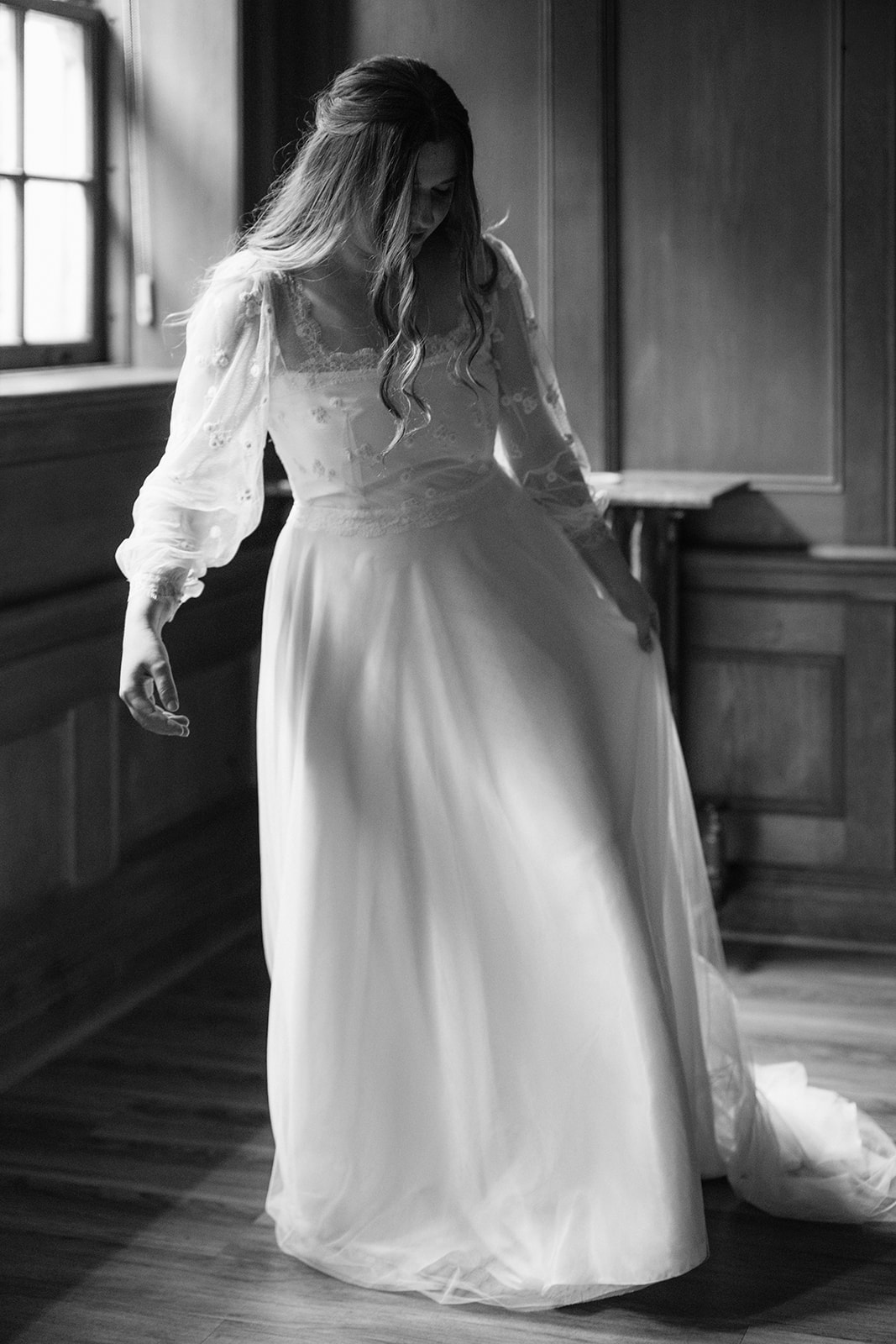 Bride adjusting her wedding dress in window light at Lairmont Manor