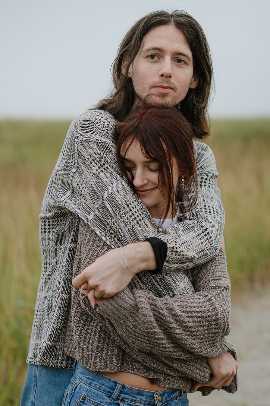 Coastal Embrace - Contentment in Oregon Engagement Photography Content couple in a close hold amidst the grassy dunes of the Oregon coast