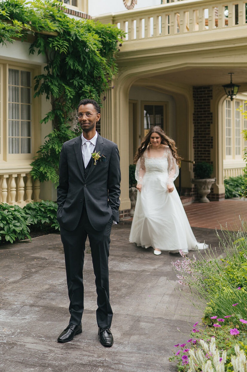 Bride approaches groom from behind for a romantic garden first look at Lairmont Manor.